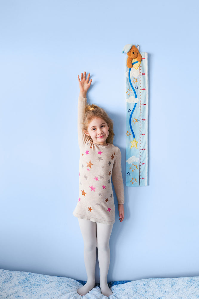 Little blonde girl measuring her height against a blue wall.