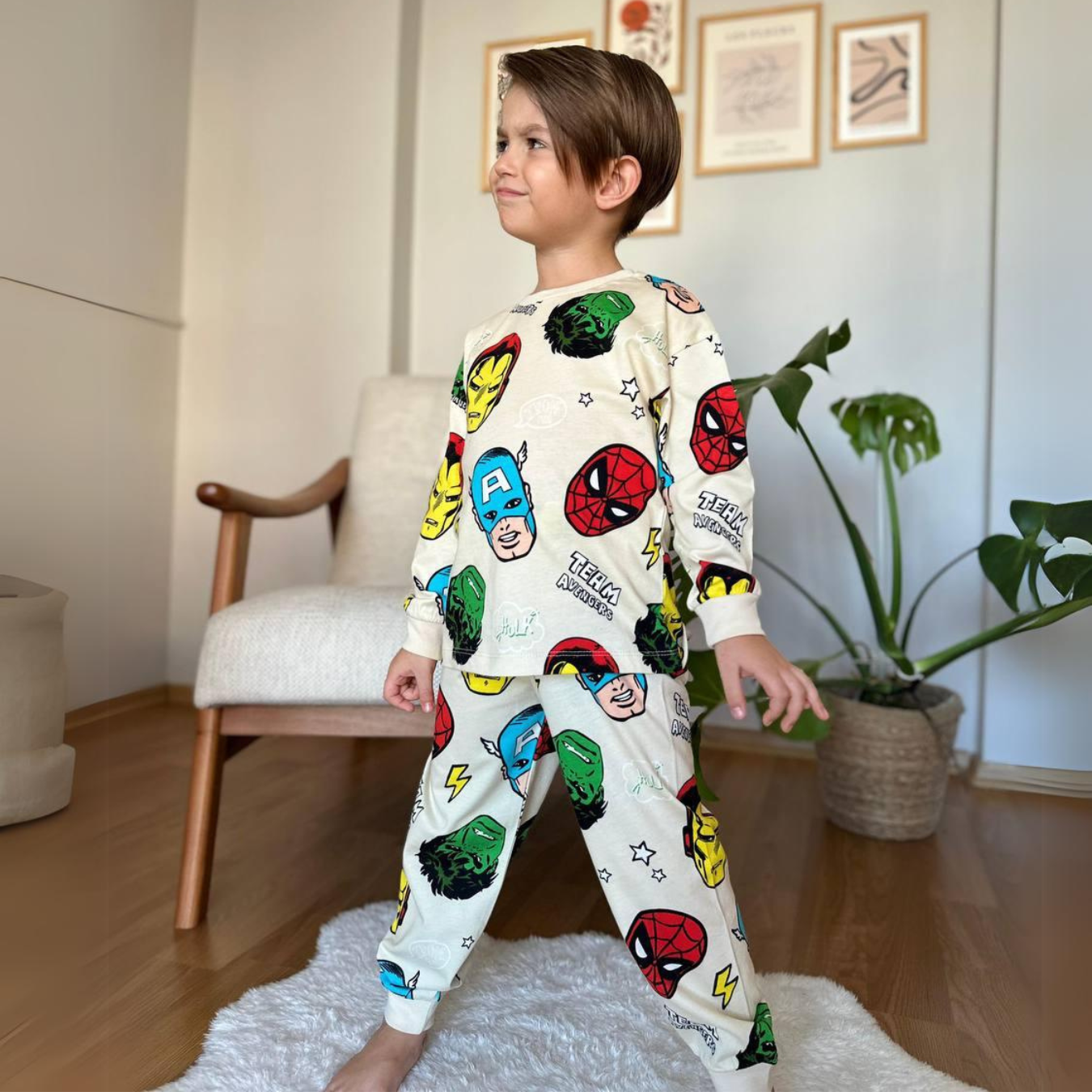 A young boy stands confidently in a cream-colored pajama set featuring Marvel superhero prints.