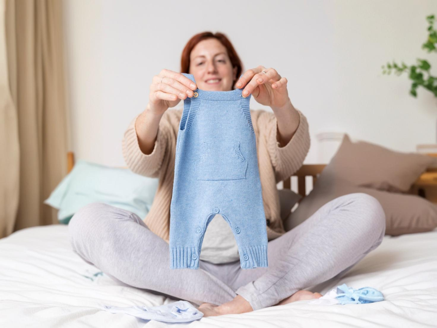 Pregnant woman holding and looking at baby clothes in a store, preparing for her newborn's arrival, and choosing essentials for her baby’s wardrobe.