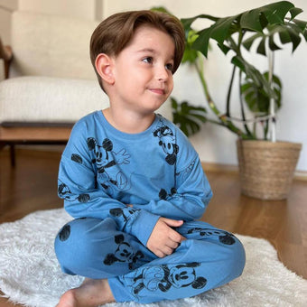 A young boy sitting on a rug wearing blue pajamas with Mickey Mouse print