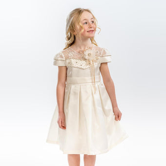 Young girl wearing an ivory satin dress with sheer embroidered neckline, floral applique, and pleated skirt.