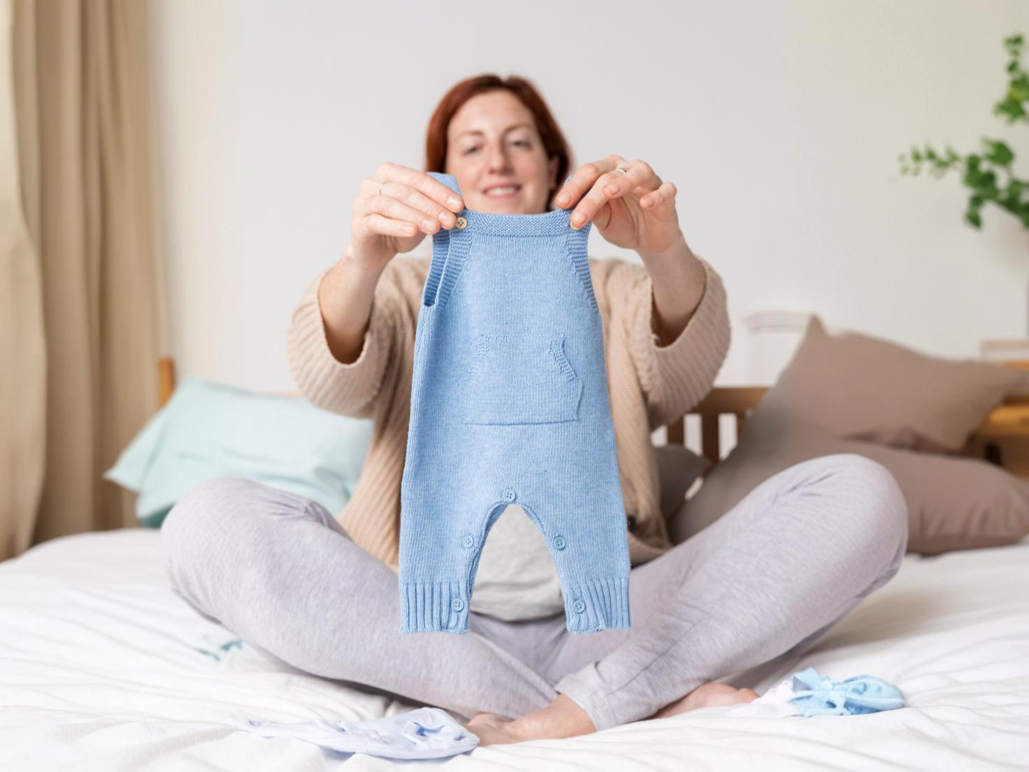  Pregnant woman holding and looking at baby clothes in a store, preparing for her newborn's arrival, and choosing essentials for her baby’s wardrobe.