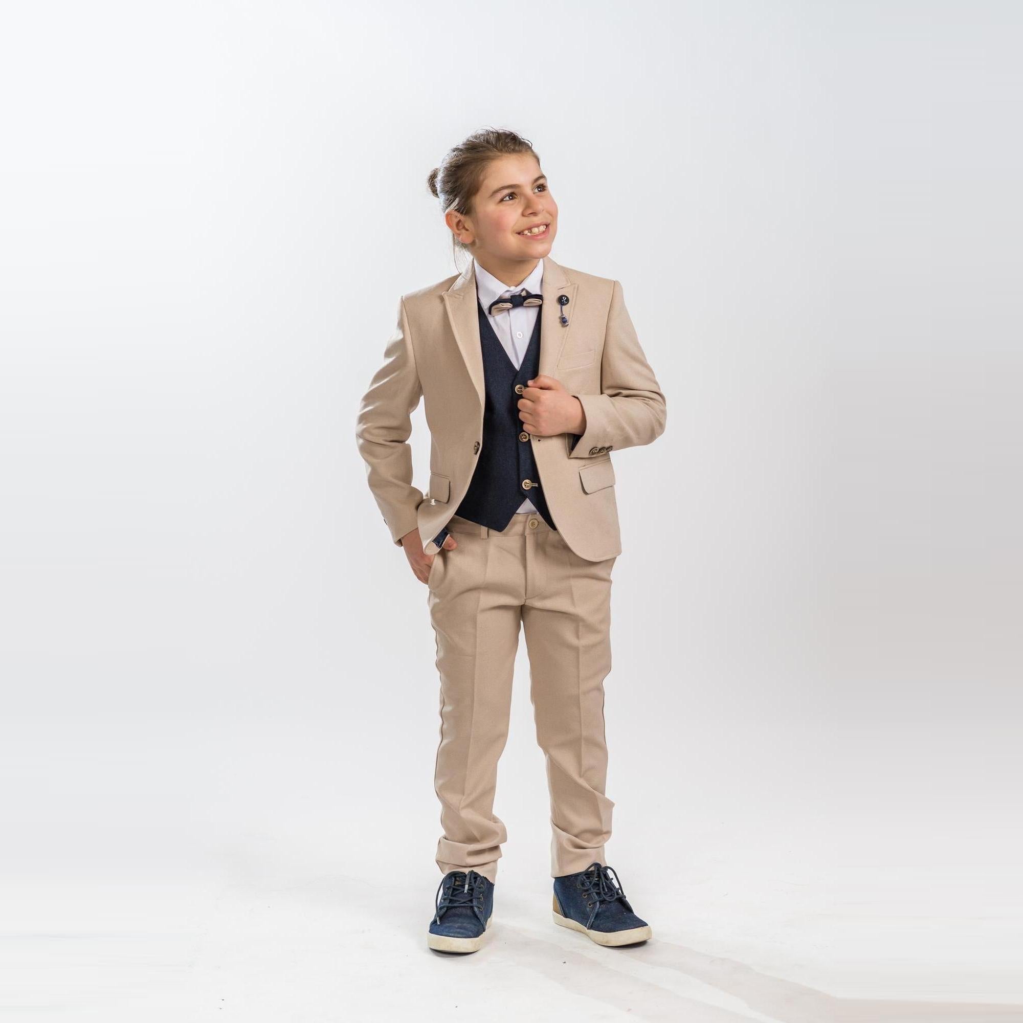 Young boy wearing a beige formal suit with matching trousers, navy vest, white shirt, and bow tie, styled for a boy's formal wear look at events.