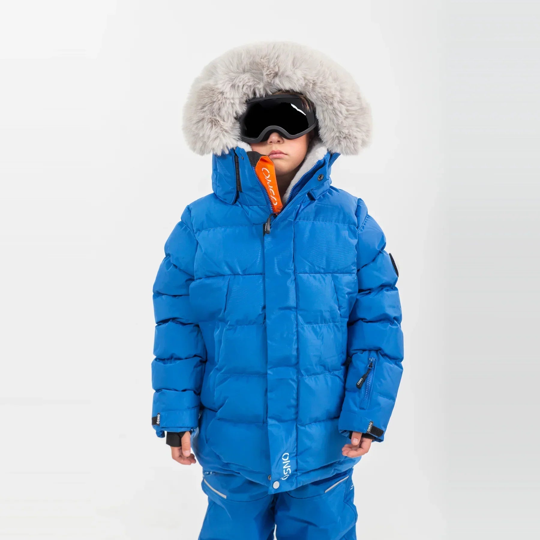  Child wearing ÖSNO blue puffer ski jacket with fur-trimmed hood and ski goggles.
