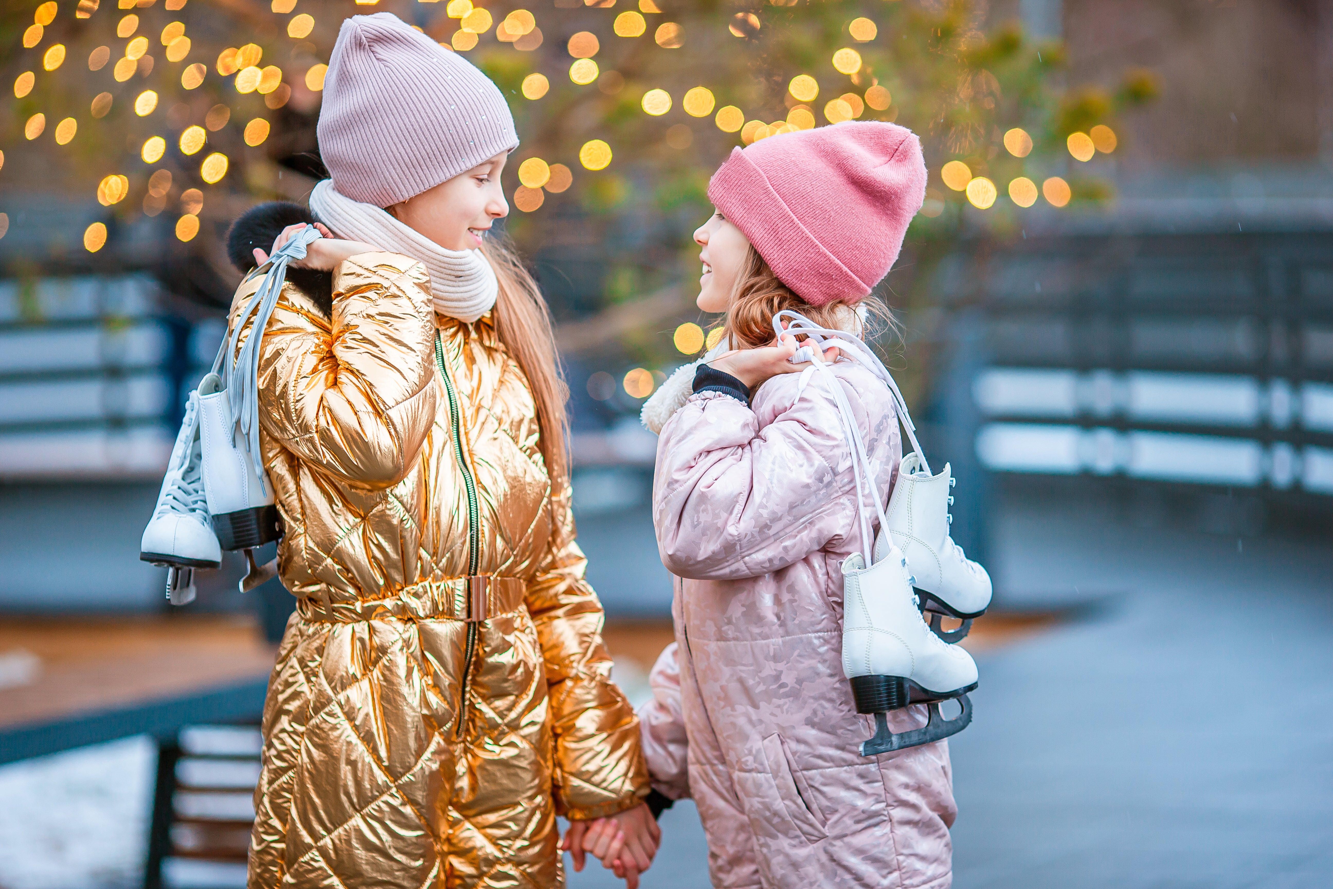 Adorable girls skating in cute winter outfits on an ice rink outdoors.