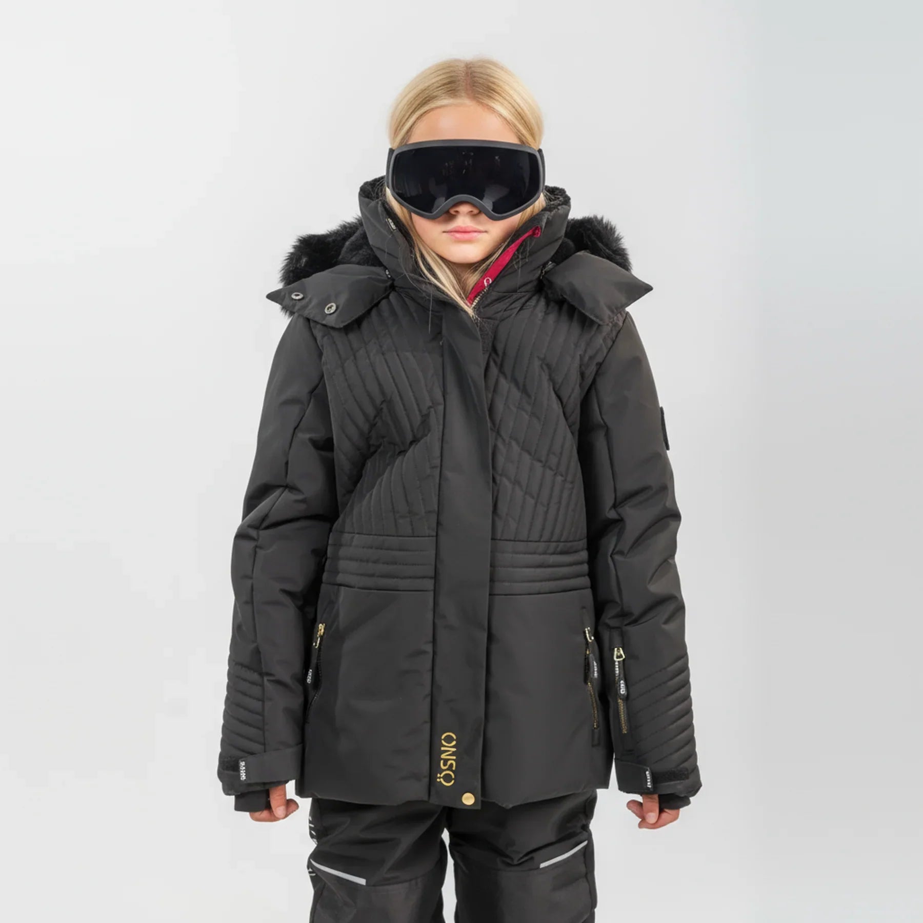 Woman wearing black ÖSNO quilted ski jacket with fur-trim hood and gold accents.