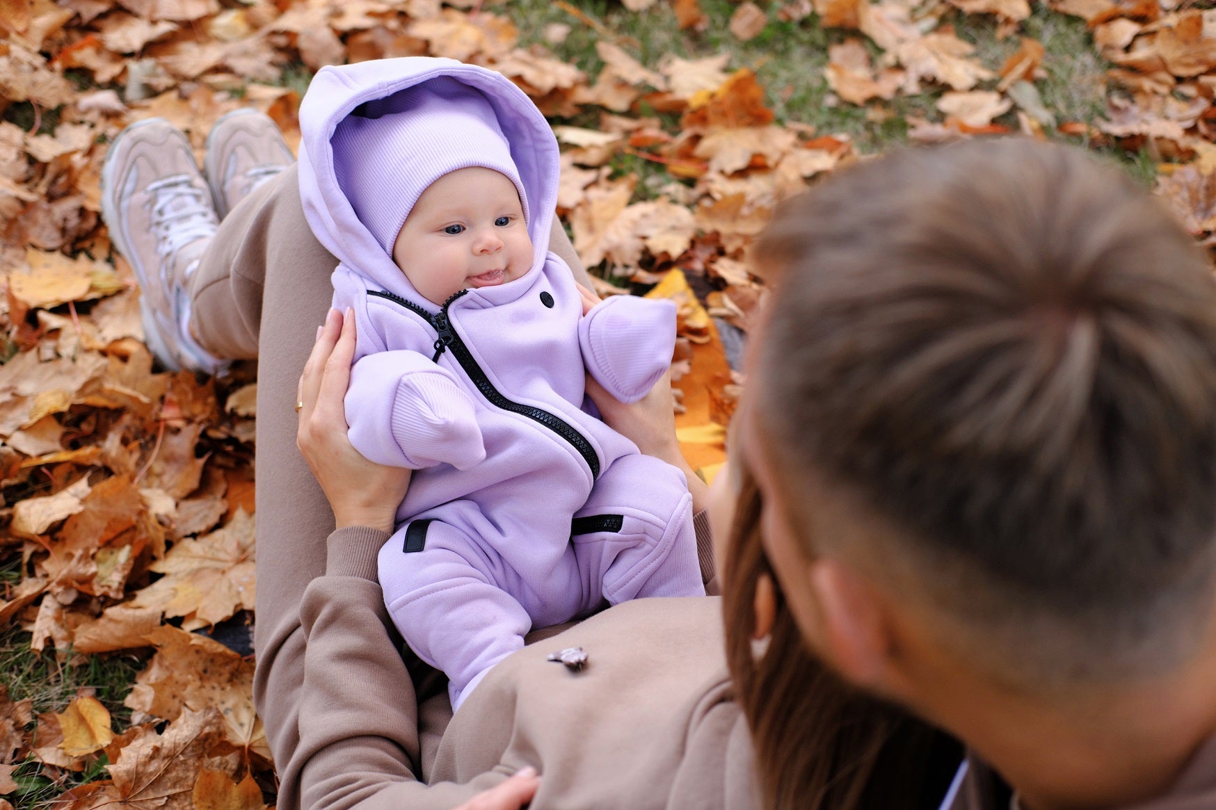 Baby in a fall outfit, resting on a parent’s lap surrounded by leaves.