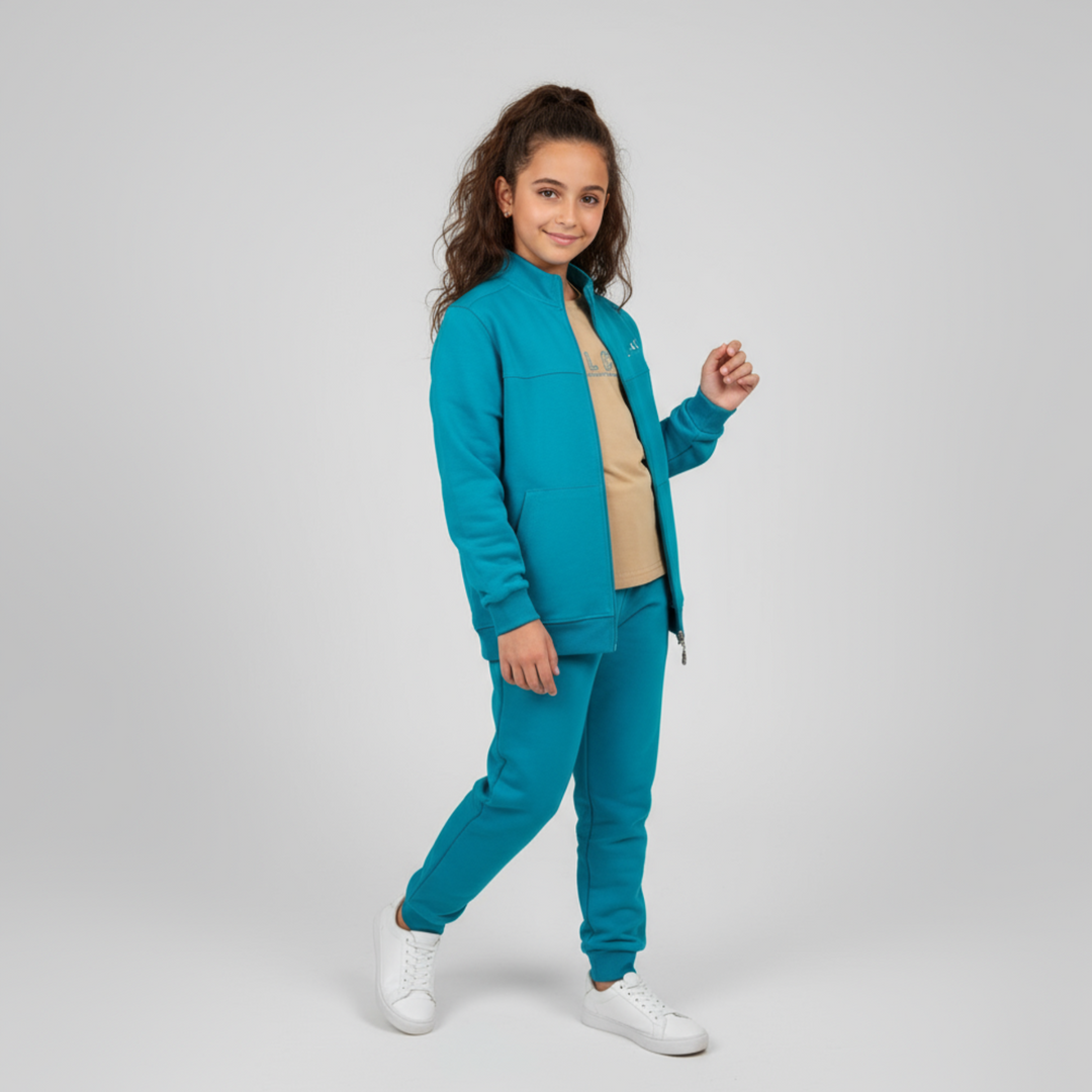 Child wearing a teal zip-up jacket with matching joggers, a beige t-shirt, and white sneakers.