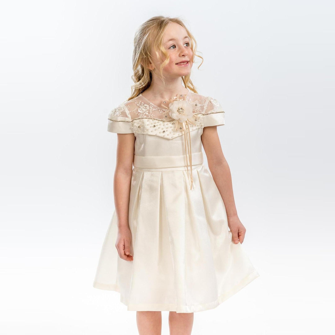 Young girl wearing an ivory satin dress with sheer embroidered neckline, floral applique, and pleated skirt.